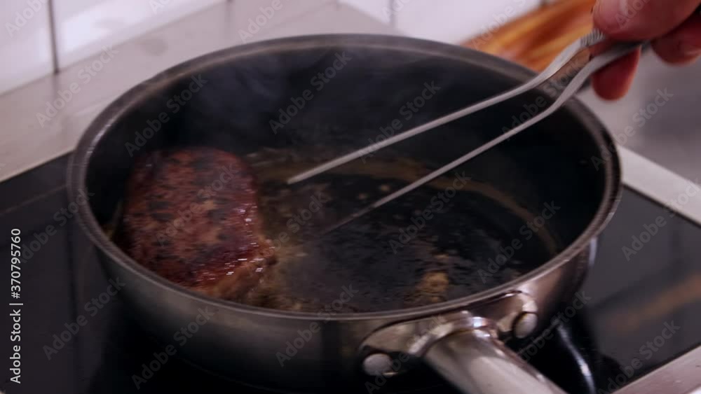 Restaurant kitchen - the chef is frying a steak in a deep pan and turns it with sticks Restaurant kitchen - the chef is frying a steak in a deep pan and turns it with sticks