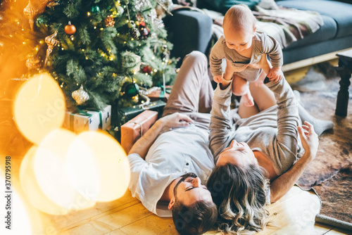 Winter time and family love. Couple in love kisses and hugs near the Christmas tree lights.