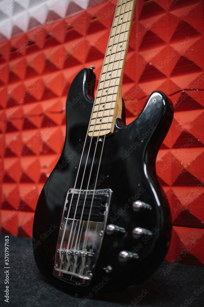Fototapeta premium Black electric guitar propped on wall in soundproof studio. Close-up portrait of shiny guitar on wall in music recording studio.