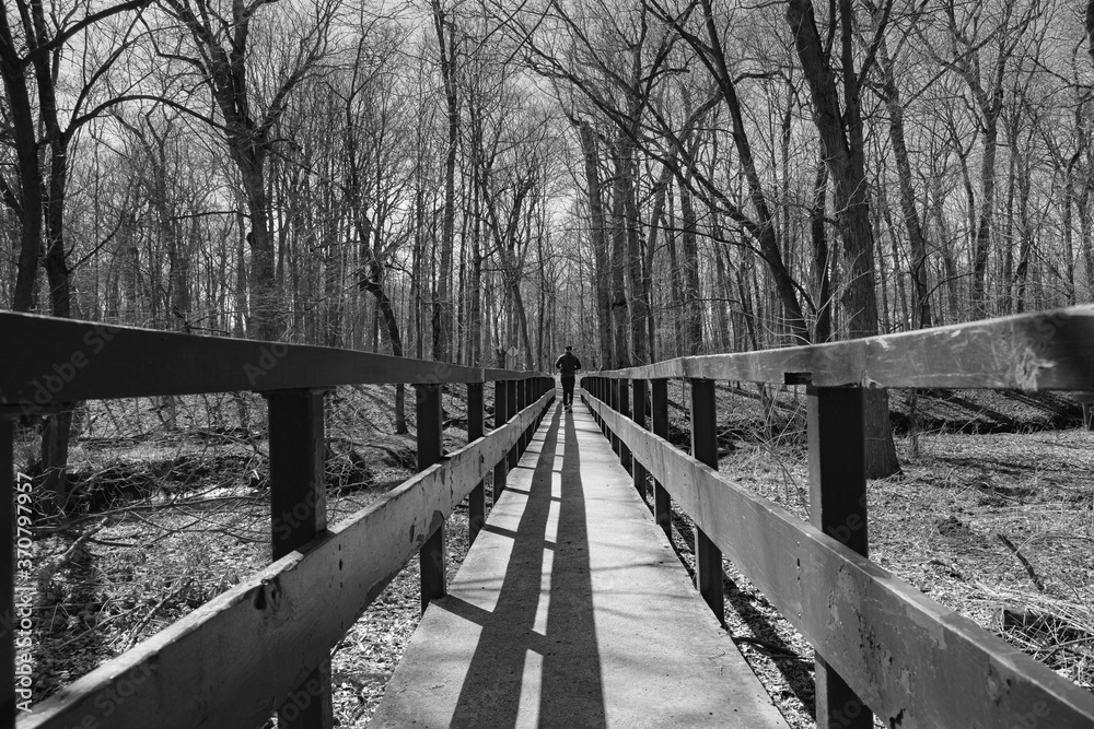Fototapeta premium Lone runner seemingly being channeled by leading lines of bridge fence and shadows