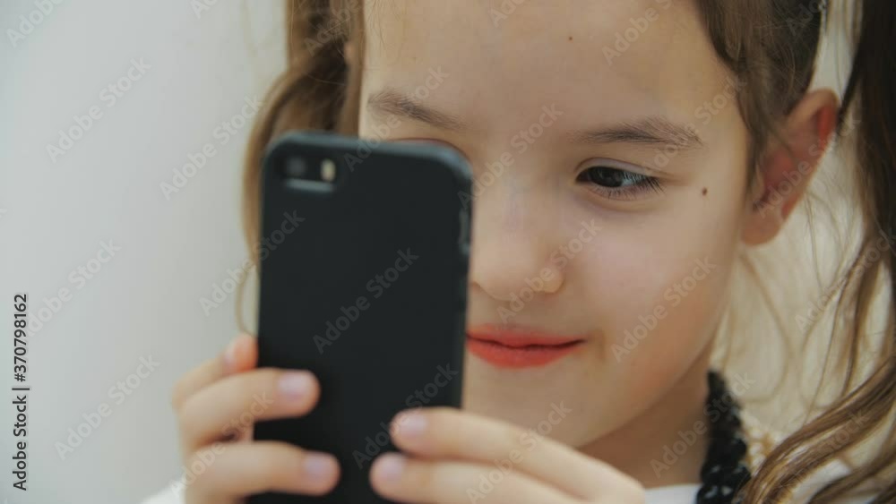 Cropped video of cute little girl with pigtails and necklace, holding black phone, taking photos. Cropped video of cute little girl with pigtails and necklace, holding black phone, taking photos.