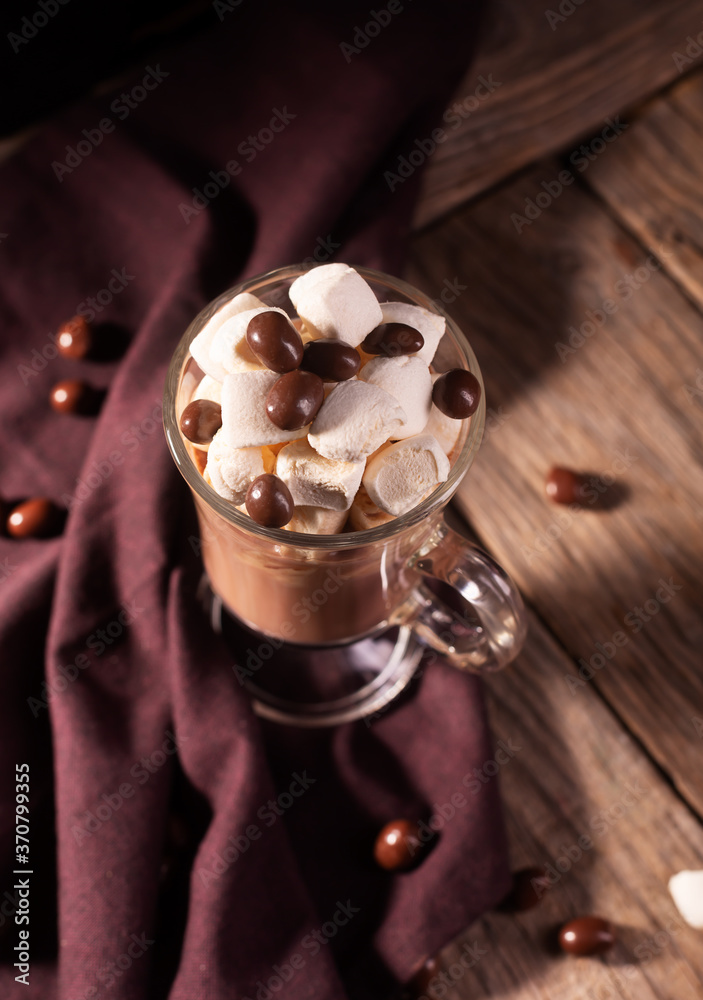 Hot chocolate with cinnamon and marshmallow on wooden background with chocolate sweets