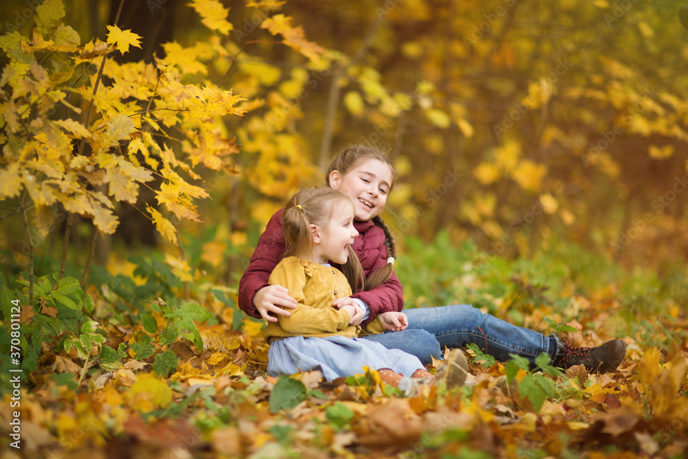 sisters sit on grass in Park against background of autumn trees. happy children laugh. walk with kids outdoor sisters sit on grass in Park against background of autumn trees. happy children laugh. walk with kids outdoor