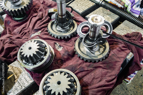 A gear wheel on a shaft with bearings of a disassembled gearbox being repaired in a workshop.