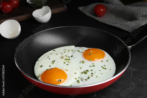 Tasty cooked eggs with herbs in frying pan on black table, closeup