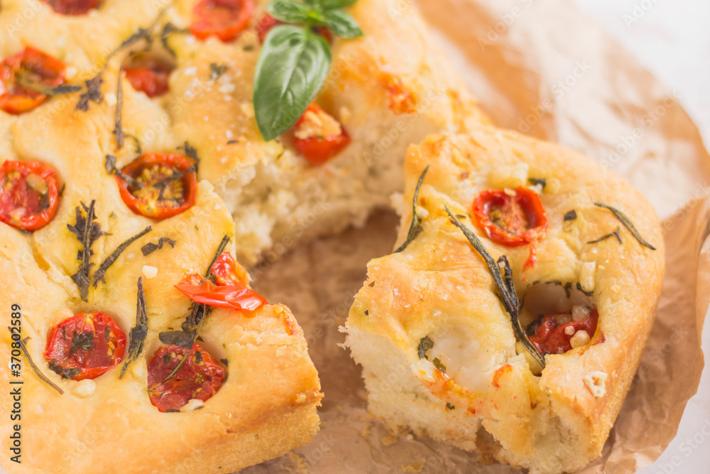 Traditional italian focaccia bread with tomatoes and rosemary in mental baking tray . On the beige brown paper and white concrete background. Traditional italian focaccia bread with tomatoes and rosemary in mental baking tray . On the beige brown paper and white concrete background.