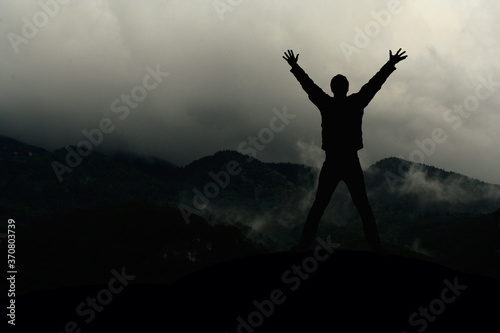 Silhouette eines Mannes mit den Armen in der Luft vor furchteinflößender Landschaft