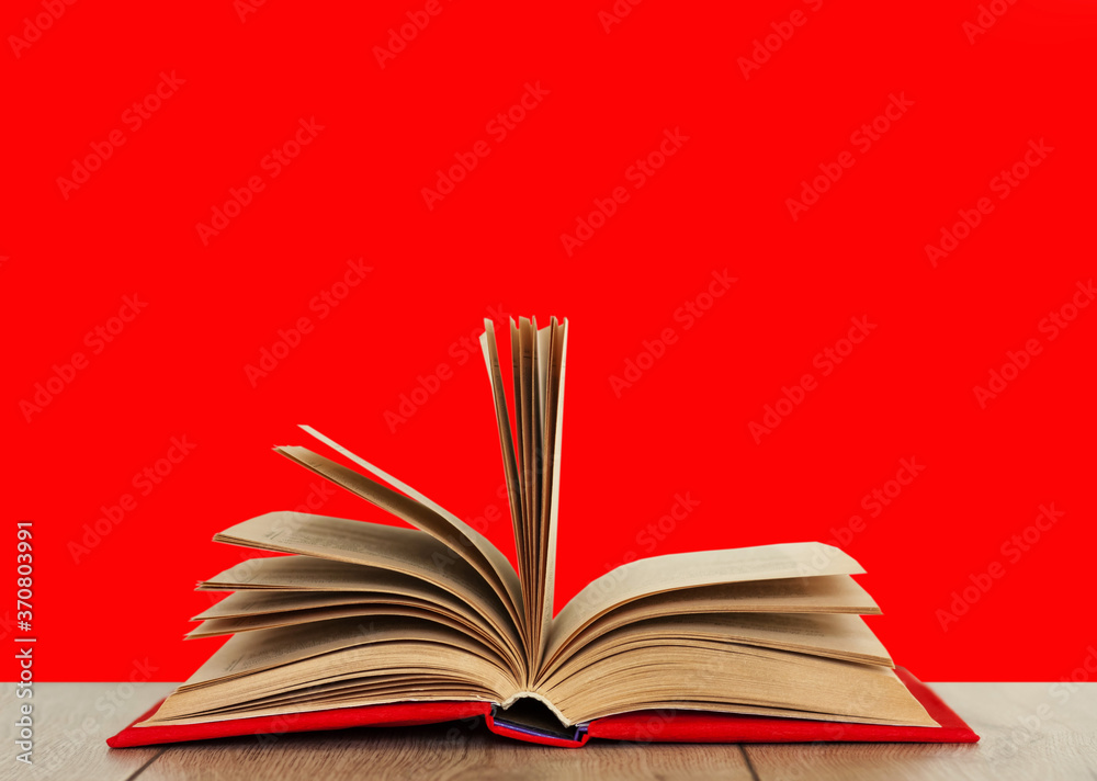 Open book textbook in a red cover on a wooden desk with red background. Back to school distance home education.Quarantine concept of stay home. Open book textbook in a red cover on a wooden desk with red background. Back to school distance home education.Quarantine concept of stay home.