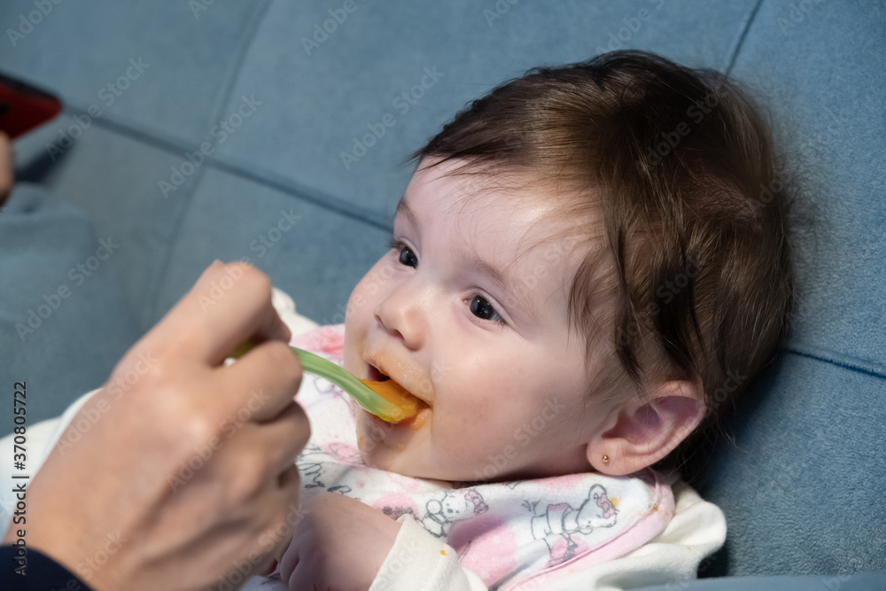 Bebê menina sorridente sendo alimentada com uma colher de plástico. Mãe cuidando da filha. Bebê menina sorridente sendo alimentada com uma colher de plástico. Mãe cuidando da filha.