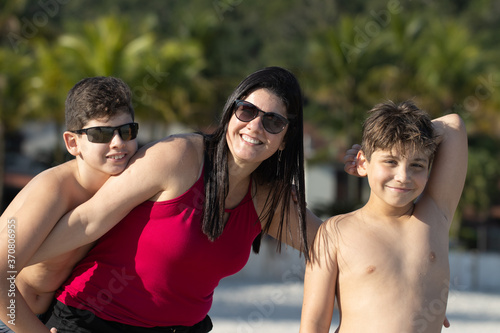 Mulher branca de cabelos pretos brincando na praia com dois meninos sorridentes. Litoral norte de São Paulo.  photo