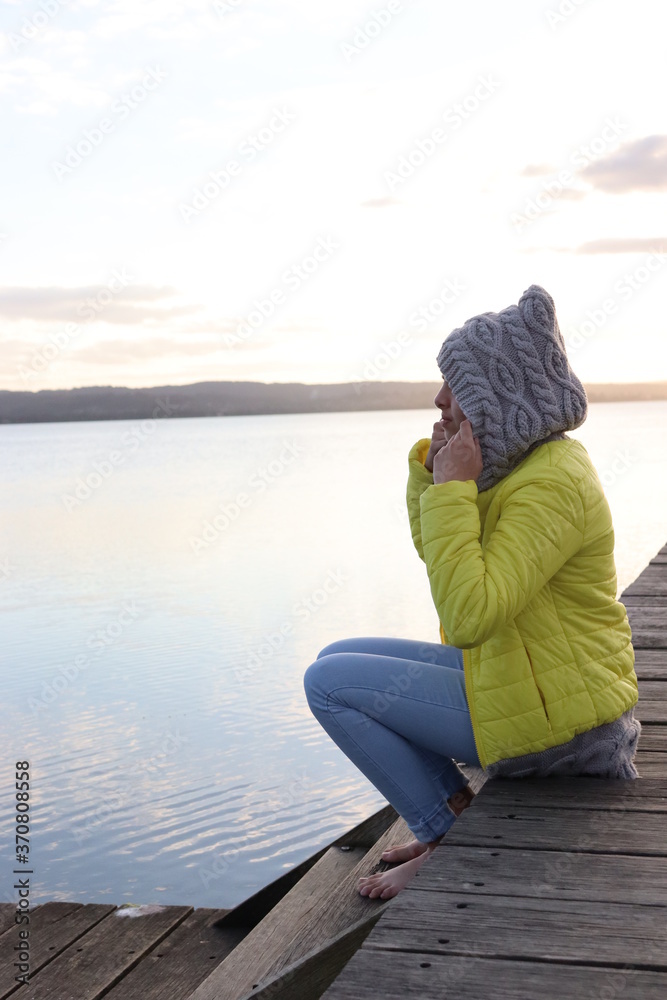 Model sitting on a boardwalk near a lake wearing yellow jacket with gray hood. Model sitting on a boardwalk near a lake wearing yellow jacket with gray hood.