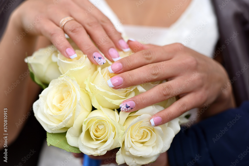 Wedding manicure on bouquet of white rose. Hands of the bride with ring.