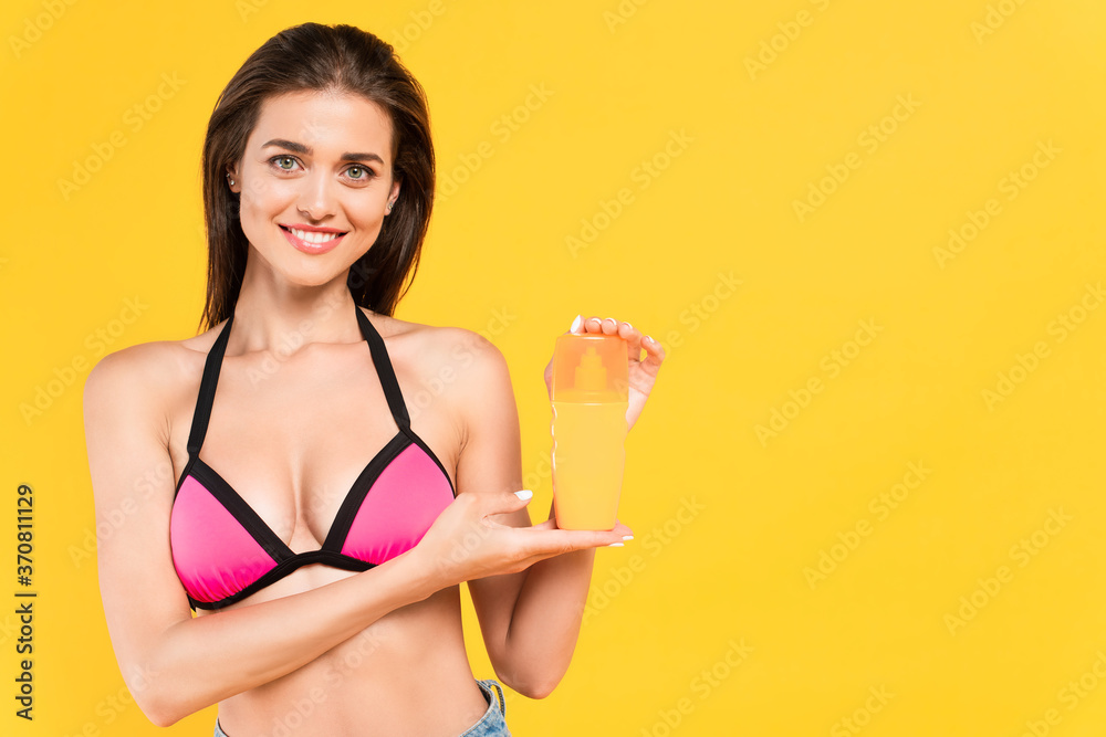 woman in swimsuit holding bottle with suntan isolated on yellow woman in swimsuit holding bottle with suntan isolated on yellow