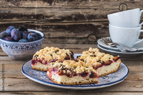 Fotografie Three pieces of plum cake with crumble on a bluewhite plate on a wooden table
