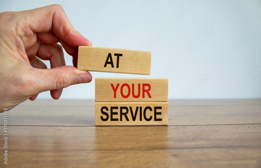 Male hand placing a block with word 'at' on top of a blocks with words 'your service'. Beautiful wooden table, white background. Copy space. Business concept. Male hand placing a block with word 'at' on top of a blocks with words 'your service'. Beautiful wooden table, white background. Copy space. Business concept.