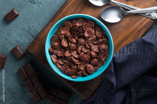 Delicious and healthy chocolate cereal in bowl with chocolate pieces laid down next to it in a dark setting