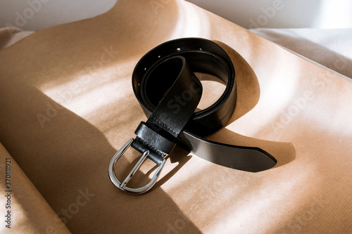 black belt with silver buckle on kraft paper, stylish belt with sun rays, shadow