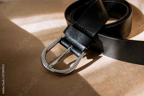 black belt with silver buckle on kraft paper, stylish belt with sun rays, shadow