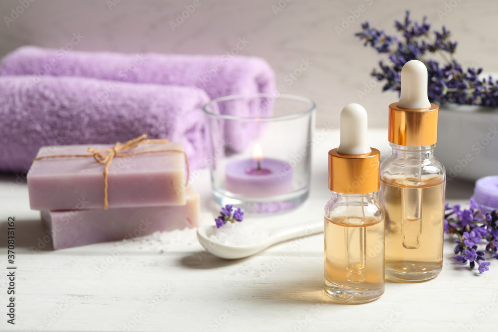 Composition with bottles of essential oil and lavender flowers on white wooden table Composition with bottles of essential oil and lavender flowers on white wooden table