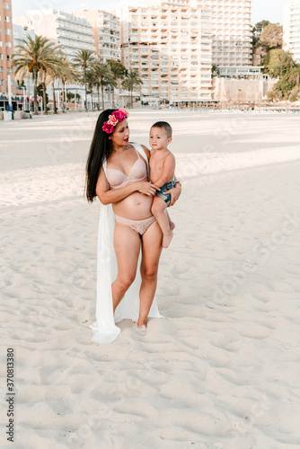 Young pregnant latin woman posing with her son in Magaluf beach. Happy family enjoying on an empty beach in Mallorca