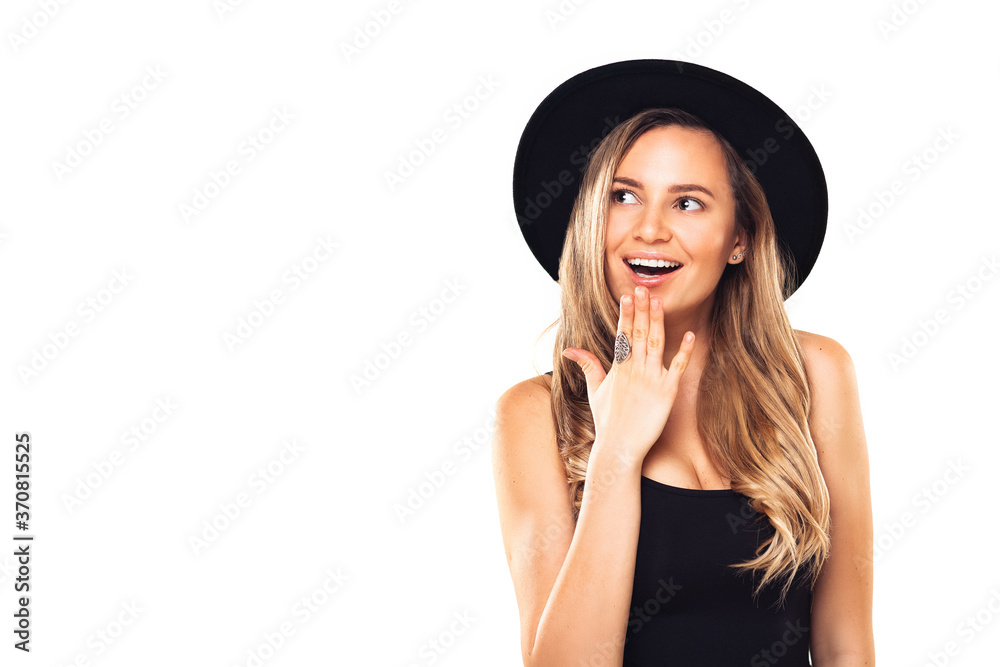 Young woman with openned mouth, happy and excited looking at copyspace. Girl with blond hair in black clothes and hat at white background Young woman with openned mouth, happy and excited looking at copyspace. Girl with blond hair in black clothes and hat at white background