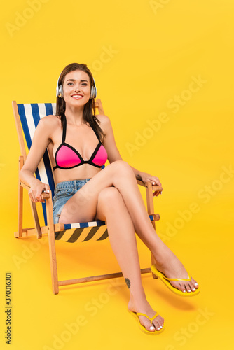  girl in swimsuit and headphones sitting on deck chair on yellow