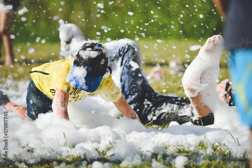 Young people in the foam. A foam party. Group of children having fun, enjoying and dancing at a foam party in aquapark. Outdoor view of foam machine.