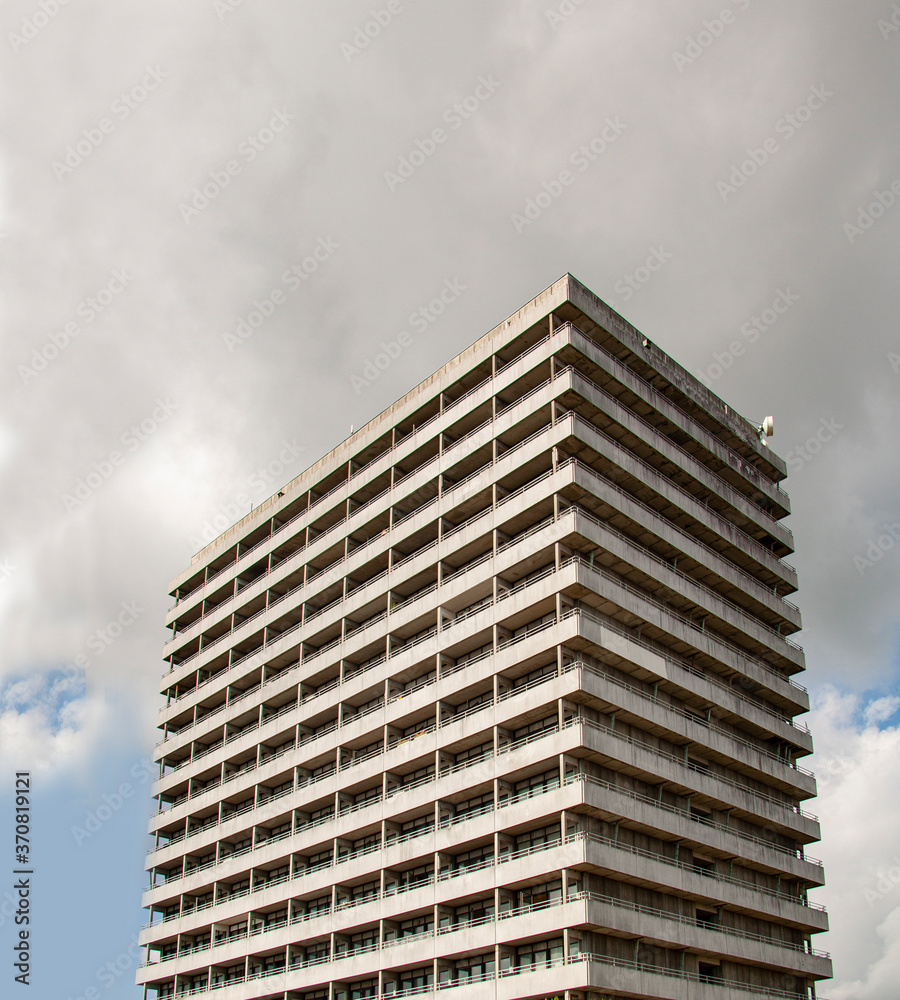 High rise residential concrete building in concrete brutalism style with heavy overcast white and gray clouds. High rise residential concrete building in concrete brutalism style with heavy overcast white and gray clouds.