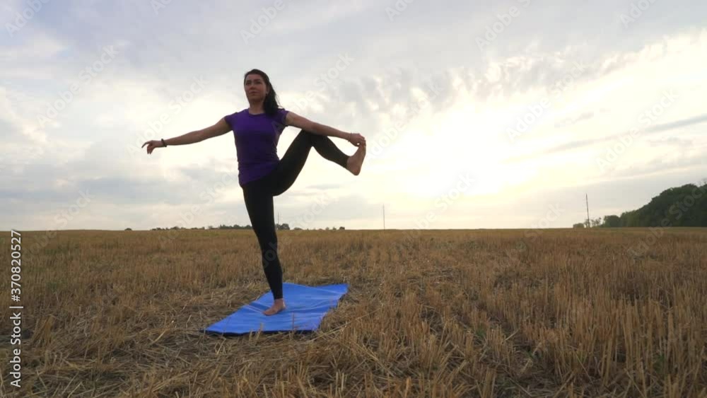 Young woman is practicing yoga outdoor on the grass at dawn. Stretching exercise on field with nature view, flexible body. Sport, fitness, health care, wellness and lifestyle concept. Young woman is practicing yoga outdoor on the grass at dawn. Stretching exercise on field with nature view, flexible body. Sport, fitness, health care, wellness and lifestyle concept.