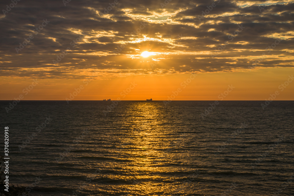 Golden sunrise at the sea on a cloudy morning. Ships can be seen against the background of sunrise on the horizon. Black sea. Sanzhiika. Ukraine