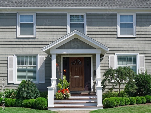 Pale green two story clapboard house with shrubbery and front lawn in summer