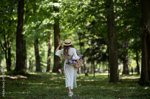 Woman with long hair and straw hat. The girl holds in her hands a wicker basket with flowers. Basket with lilacs. Woman and flowers. Walk with a basket of lilacs in the hands. Floristics.