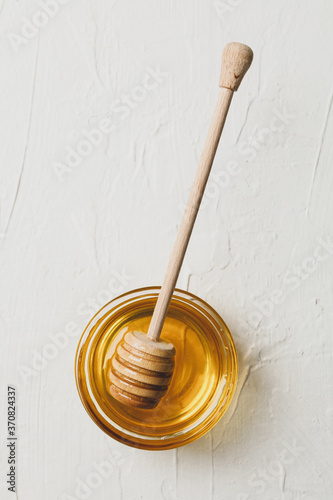 Bowl with honey and dipper on white background, top view