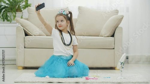 Beautiful little kid wearing crown, dress, necklace, and taking selfie, posing.