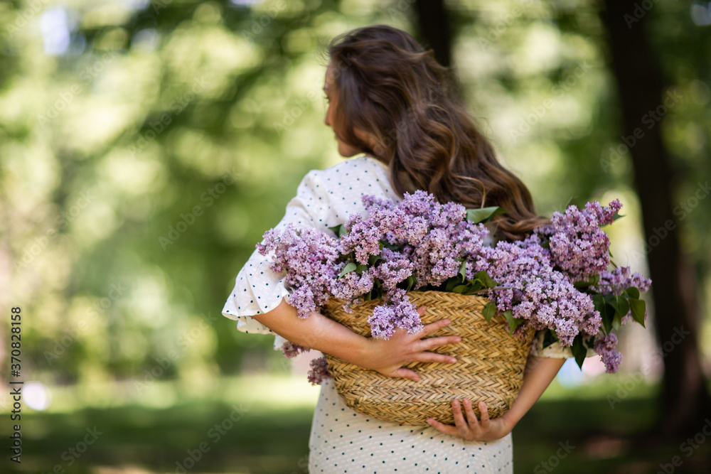 The girl holds in her hands a wicker basket with flowers. Basket with lilacs. Girl and flowers. Walk with a basket of lilacs in the hands. Floristics. Cozy atmosphere with fresh, fragrant flowers. The girl holds in her hands a wicker basket with flowers. Basket with lilacs. Girl and flowers. Walk with a basket of lilacs in the hands. Floristics. Cozy atmosphere with fresh, fragrant flowers.