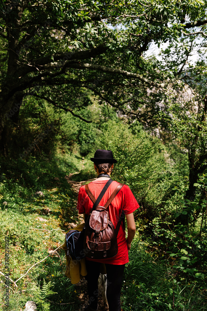 Back view of faceless female traveler with backpack walking along empty pathway surrounded by green trees on sunny day Back view of faceless female traveler with backpack walking along empty pathway surrounded by green trees on sunny day