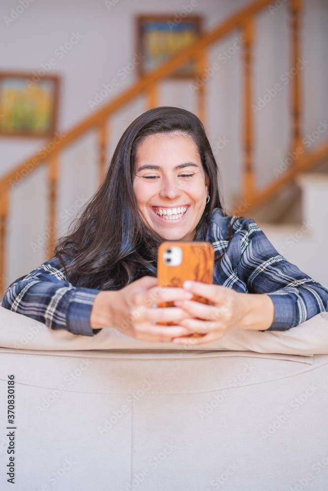 Happy youthful female in casual outfit lying on sofa and browsing internet on smartphone while chilling in cozy living room Happy youthful female in casual outfit lying on sofa and browsing internet on smartphone while chilling in cozy living room
