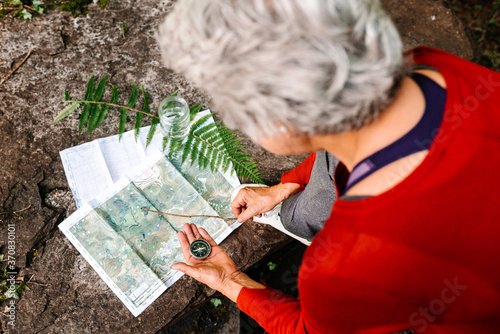 From above of anonymous female tourist orientating on map and compass while standing on rock in forest photo