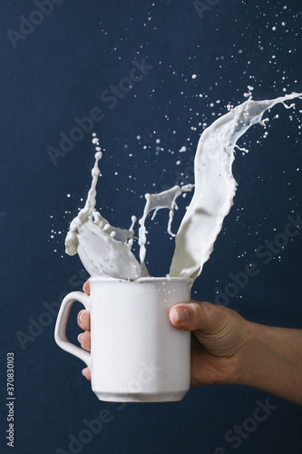 Crop female with mug of splashing milk on blue background in studio photo