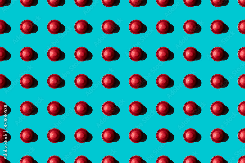 Top view of red coffee pods placed in even rows as seamless pattern on blue background Top view of red coffee pods placed in even rows as seamless pattern on blue background