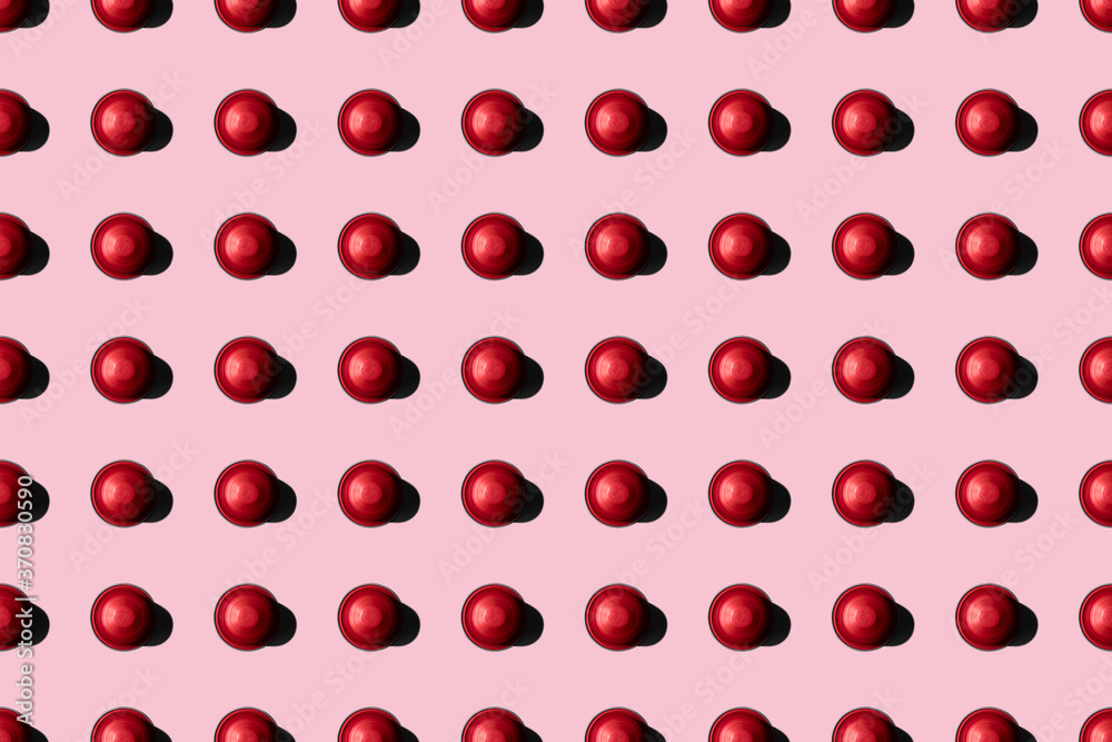 Top view of red coffee pods placed in even rows as seamless pattern on pink background Top view of red coffee pods placed in even rows as seamless pattern on pink background