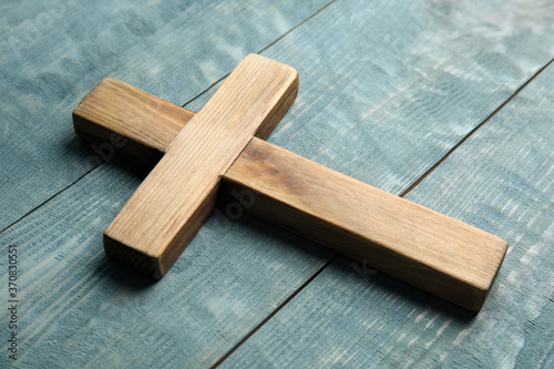 Christian cross on light blue wooden background, closeup. Religion concept