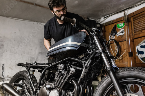 Low angle of brutal male mechanic standing in shabby workshop and repairing motorbike