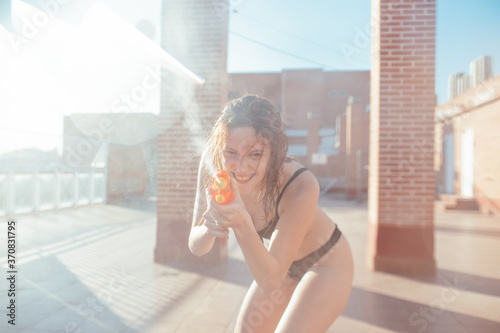 Playful female with wet hair and in swimwear having fun with water pistol on sunny day in summer looking at camera photo