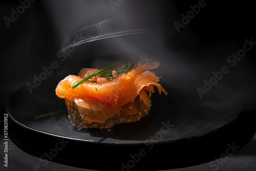 Smoked salmon and fennel herb on top of seeded bread on a dark plate and dark table