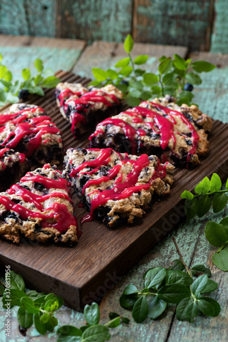 Blueberry scones with raspberry jam topping on oak cutboard with blueberry leaves on old painted wood background