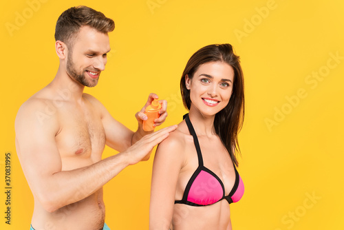 man smiling while applying sunblock on cheerful woman isolated on yellow