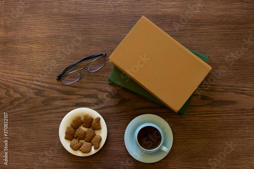 Cup of coffee, cookies,and glasses on wooden table, book top view and space for text. Break time