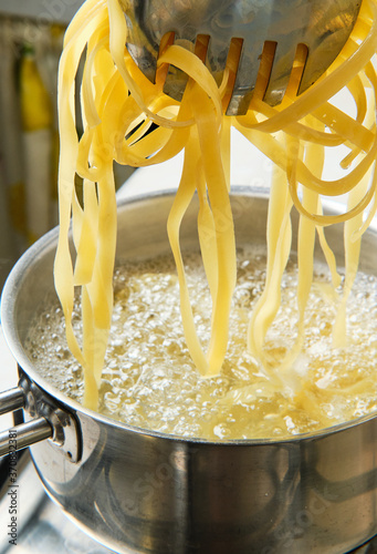 From above of delicious Italian pasta on metal tweezers pulled out of stainless steel pot with water forming bubbles and foam on surface in kitchen