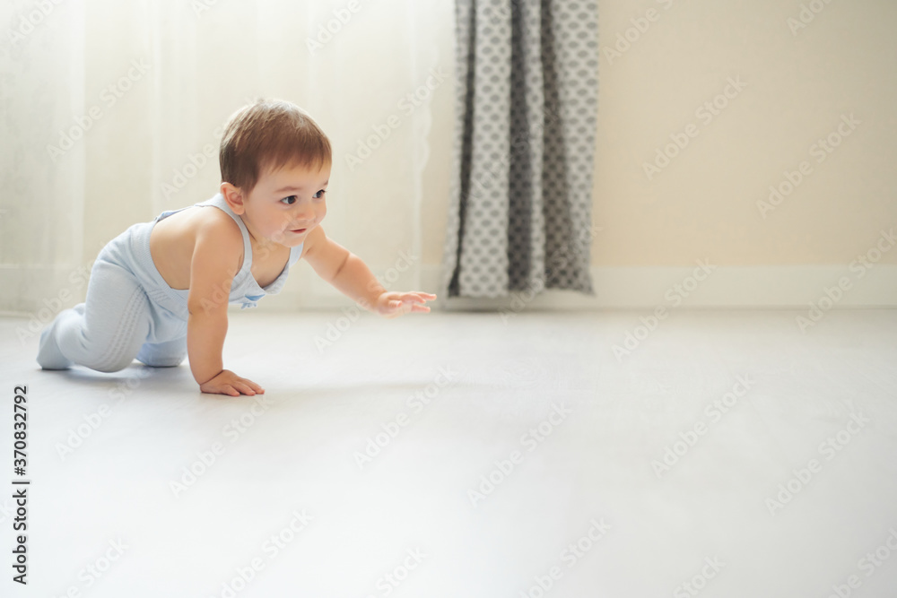 Side view of adorable little baby in gray bodysuit smiling while crawling on floor in cozy room at home Side view of adorable little baby in gray bodysuit smiling while crawling on floor in cozy room at home